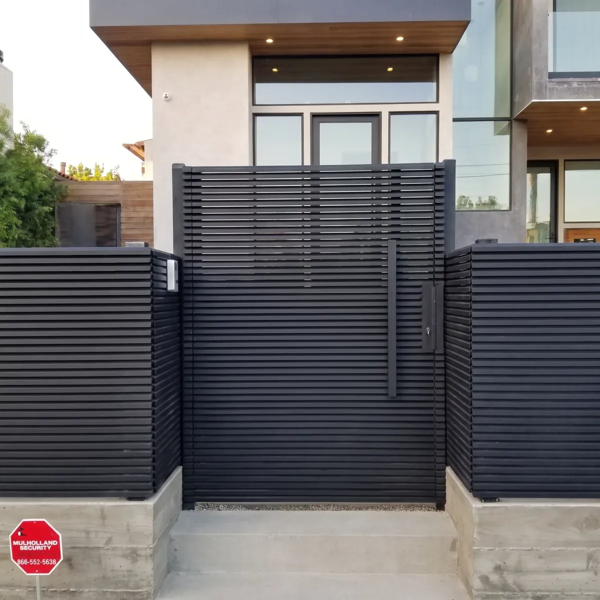 A black horizontal-slat aluminum gate and matching fence at the entrance to a modern home.