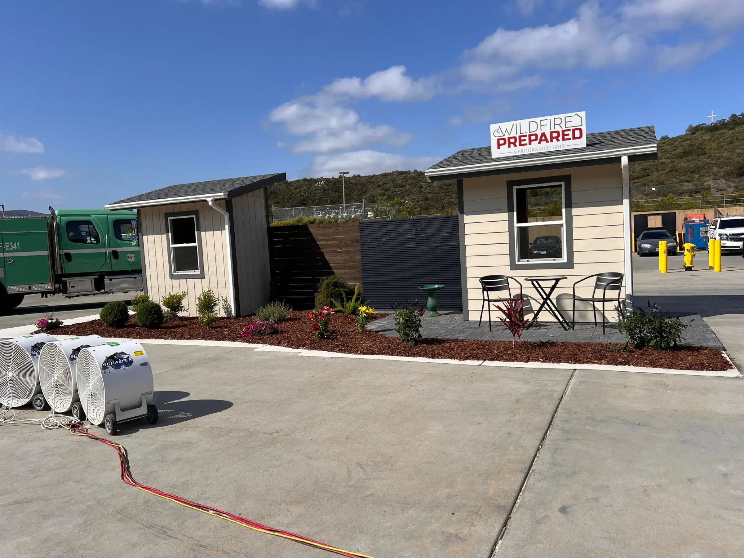 Two IBHS Wildfire Prepared test houses with a Mulholland aluminum slat screen between them, wind machines lined up before the burn test begins