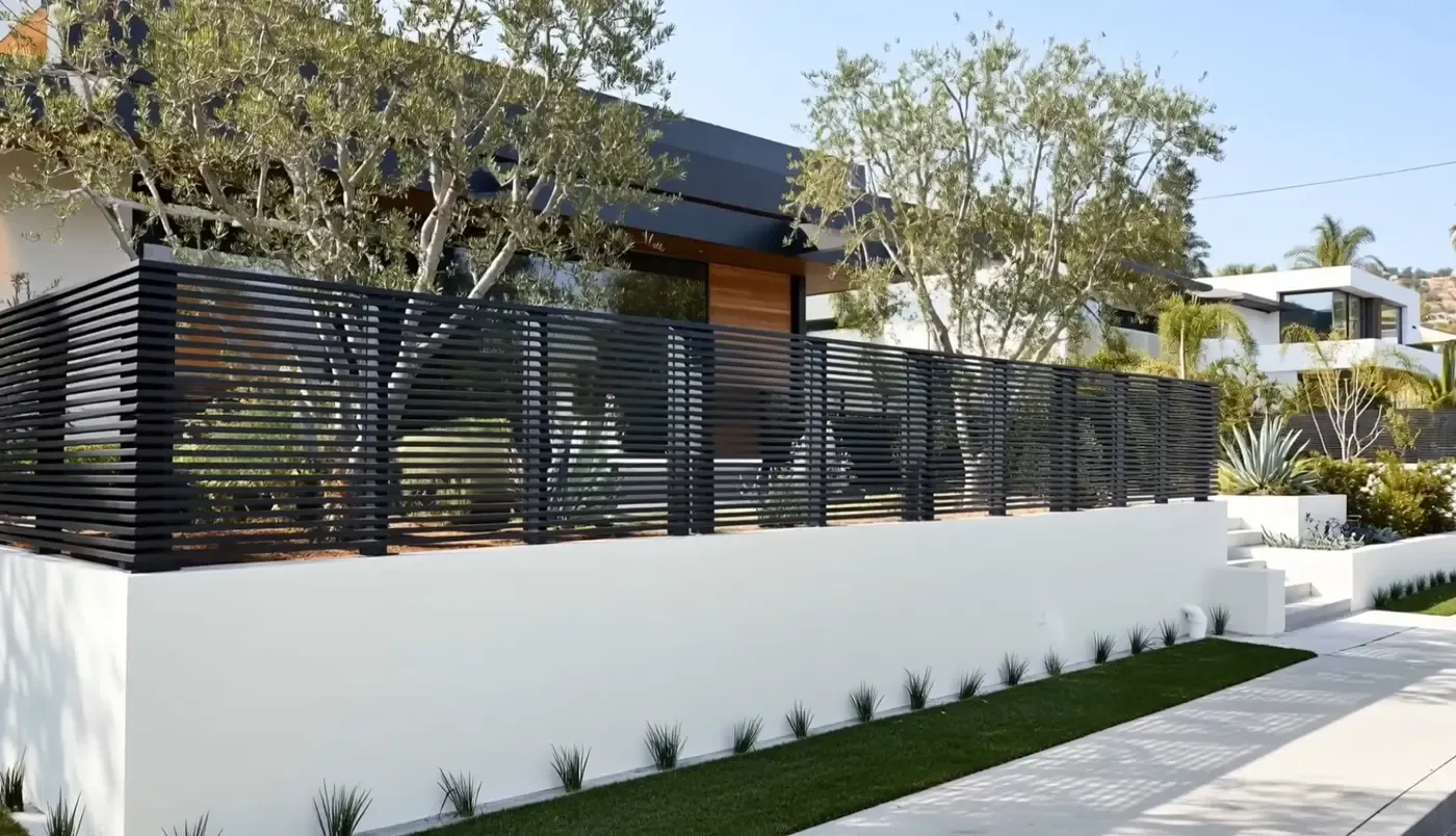 A low dark aluminum slat fence along a white garden wall in front of a modern house