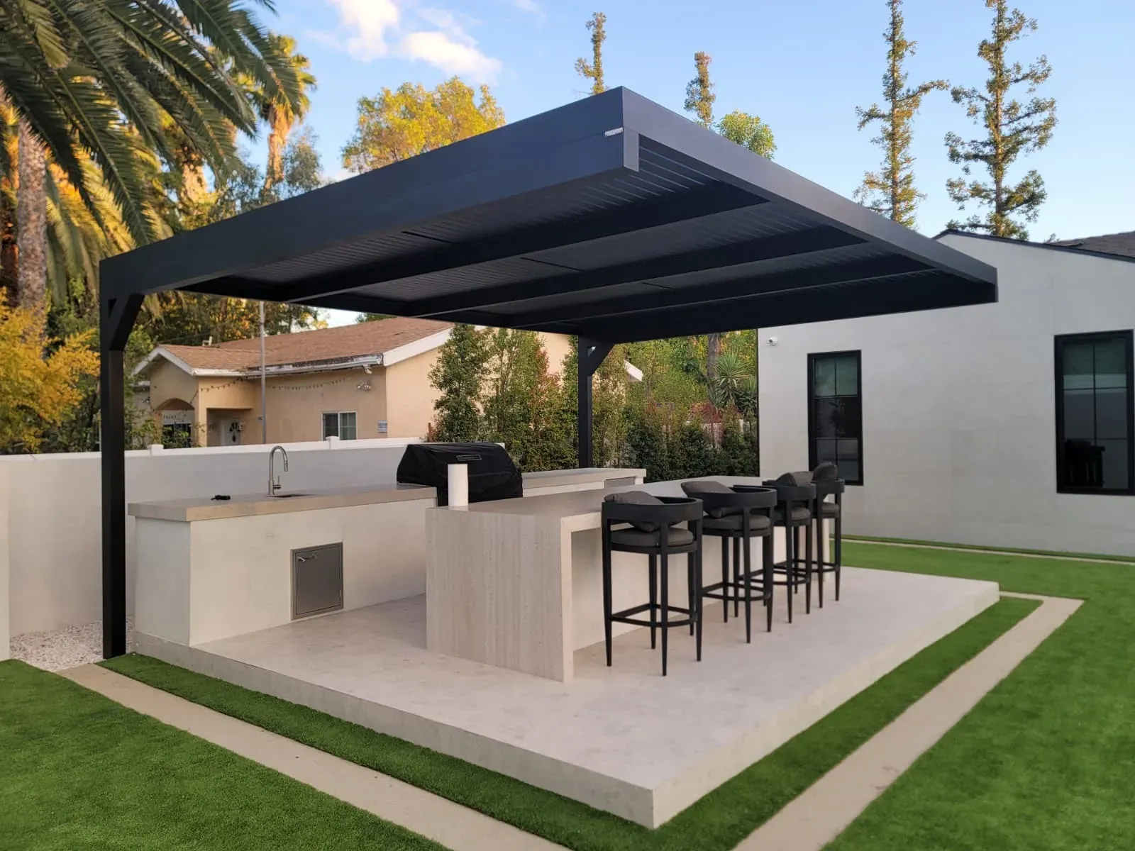 A black aluminum pergola over an outdoor kitchen with a bar counter and stools