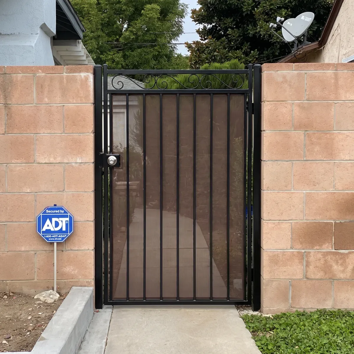 A black wrought-iron side gate with a scrolled top panel, set in a block wall.