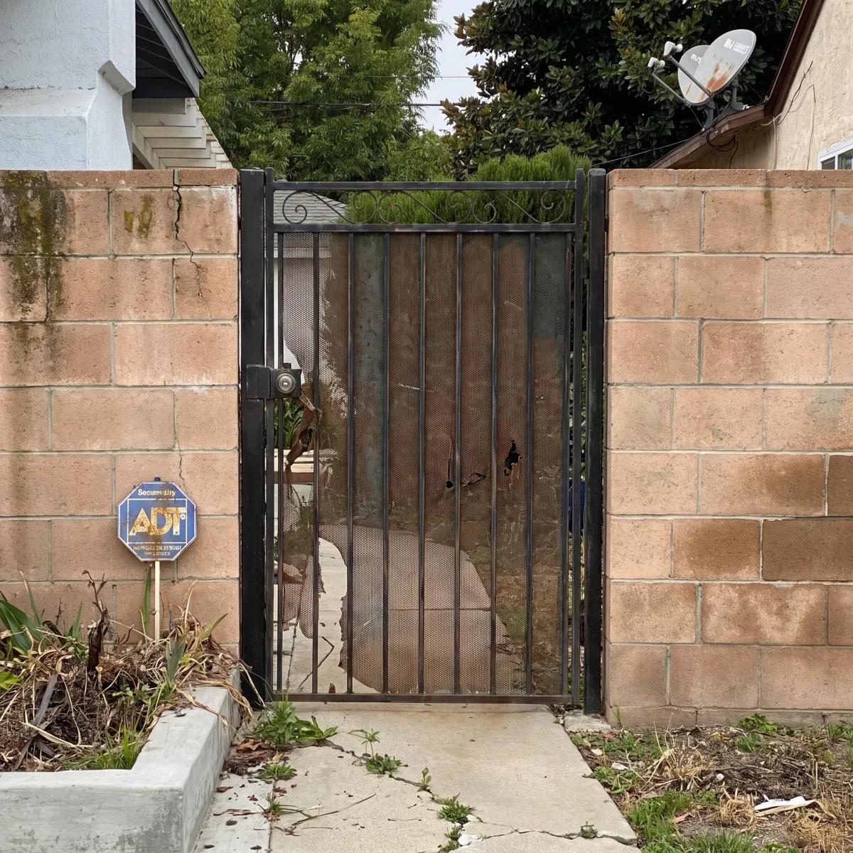 The same iron gate corroded: the paint gone to rust, the infill panel pitted and holed, the wall stained and cracked.