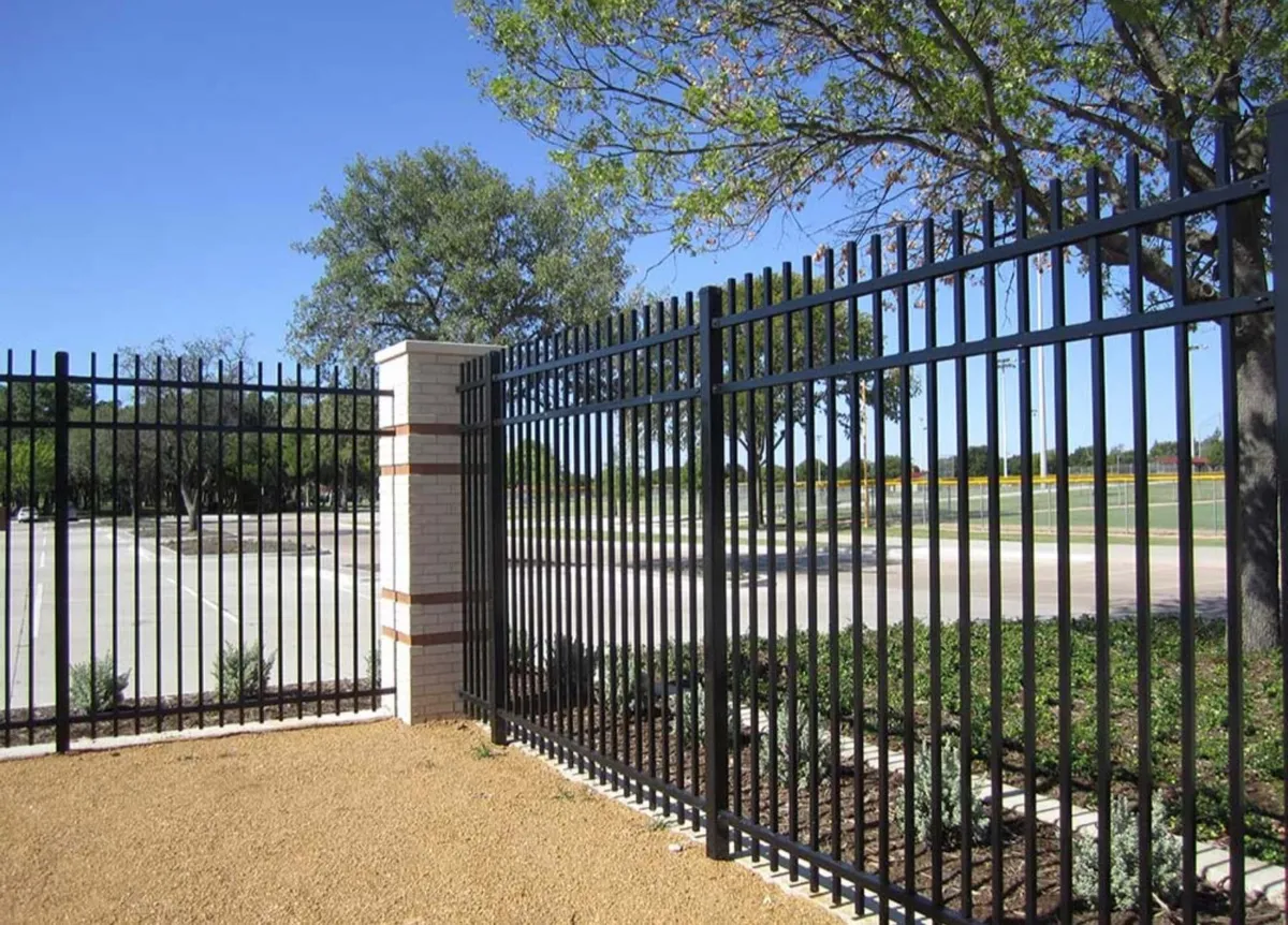 A black steel picket fence with square pickets, running from a rendered pillar along a gravel verge.