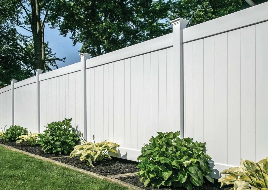 A white vinyl privacy fence in a residential garden, with shrubs planted along its base.