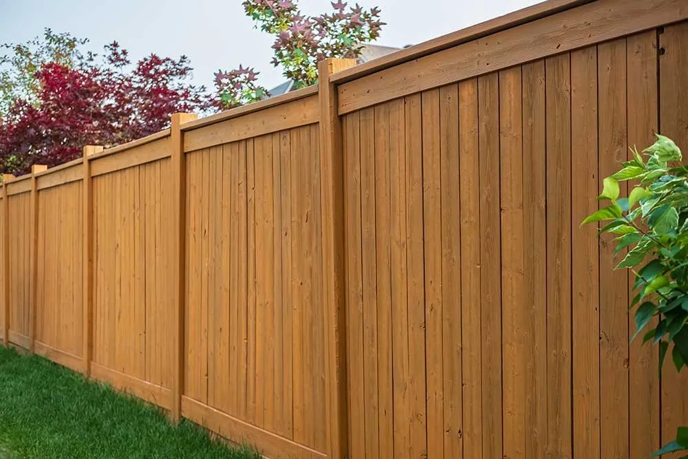 A tall wood privacy fence with vertical boards, running alongside a planted garden bed.