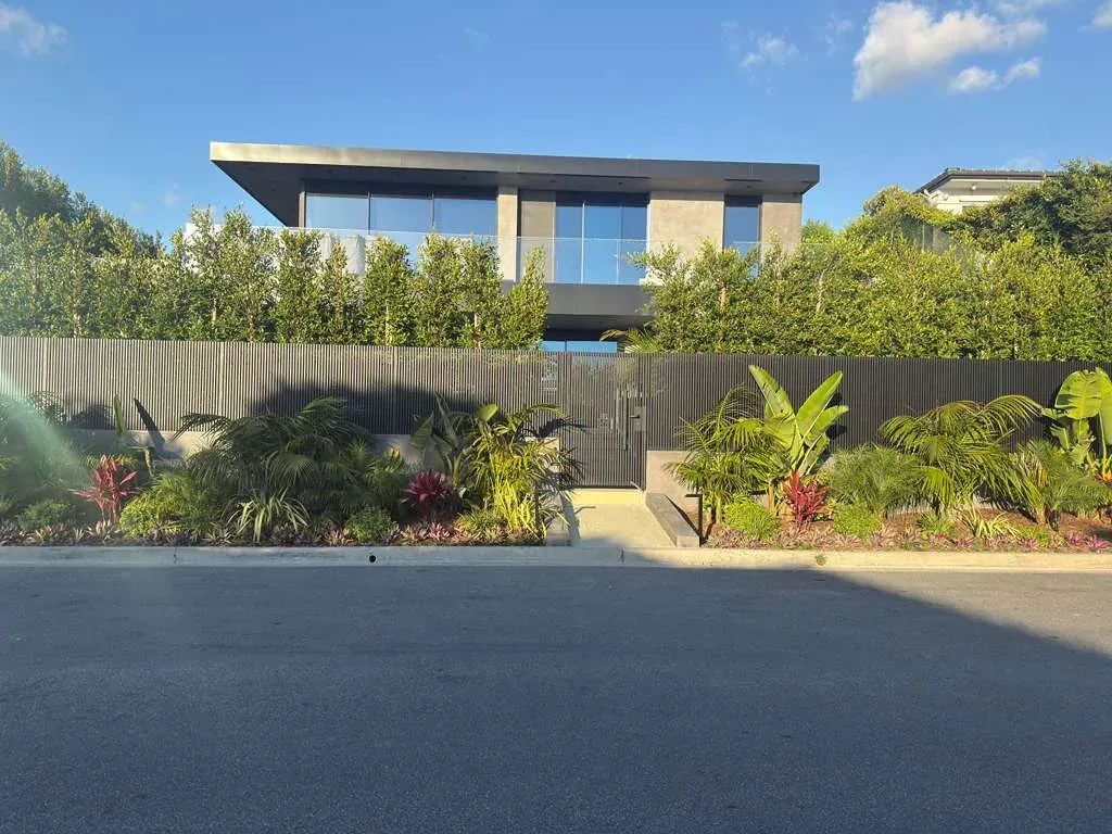 A contemporary home behind a dark aluminum fence, seen from the driveway