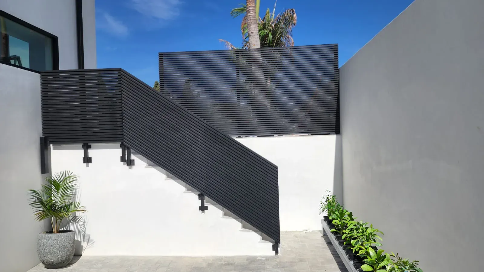 Dark aluminum slat fencing and a matching stair railing against white stucco walls