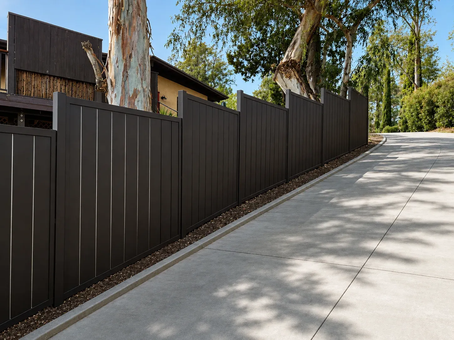 Solid dark aluminum fence panels stepping down alongside a sloping concrete driveway