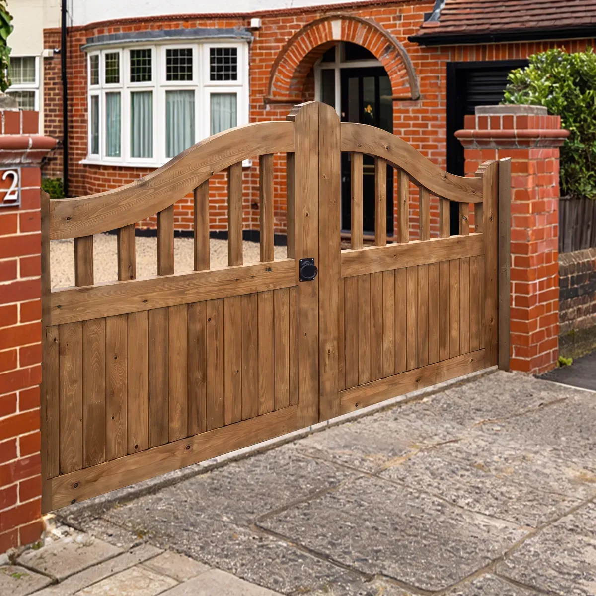 A newly stained timber driveway gate with a curved top rail, in front of a brick house.