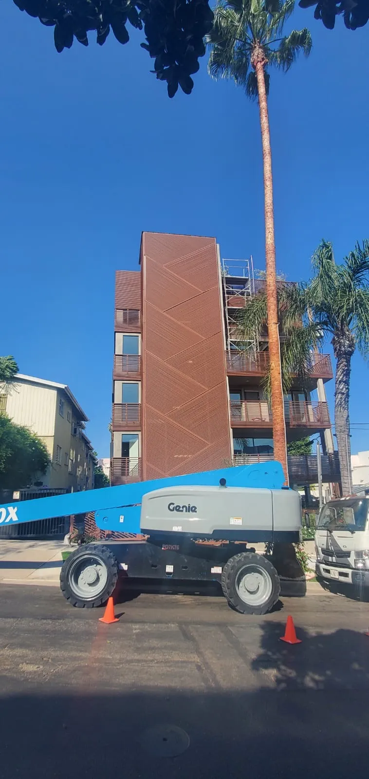 A boom lift parked in the street in front of the building, mid-installation of its perforated aluminum facade.