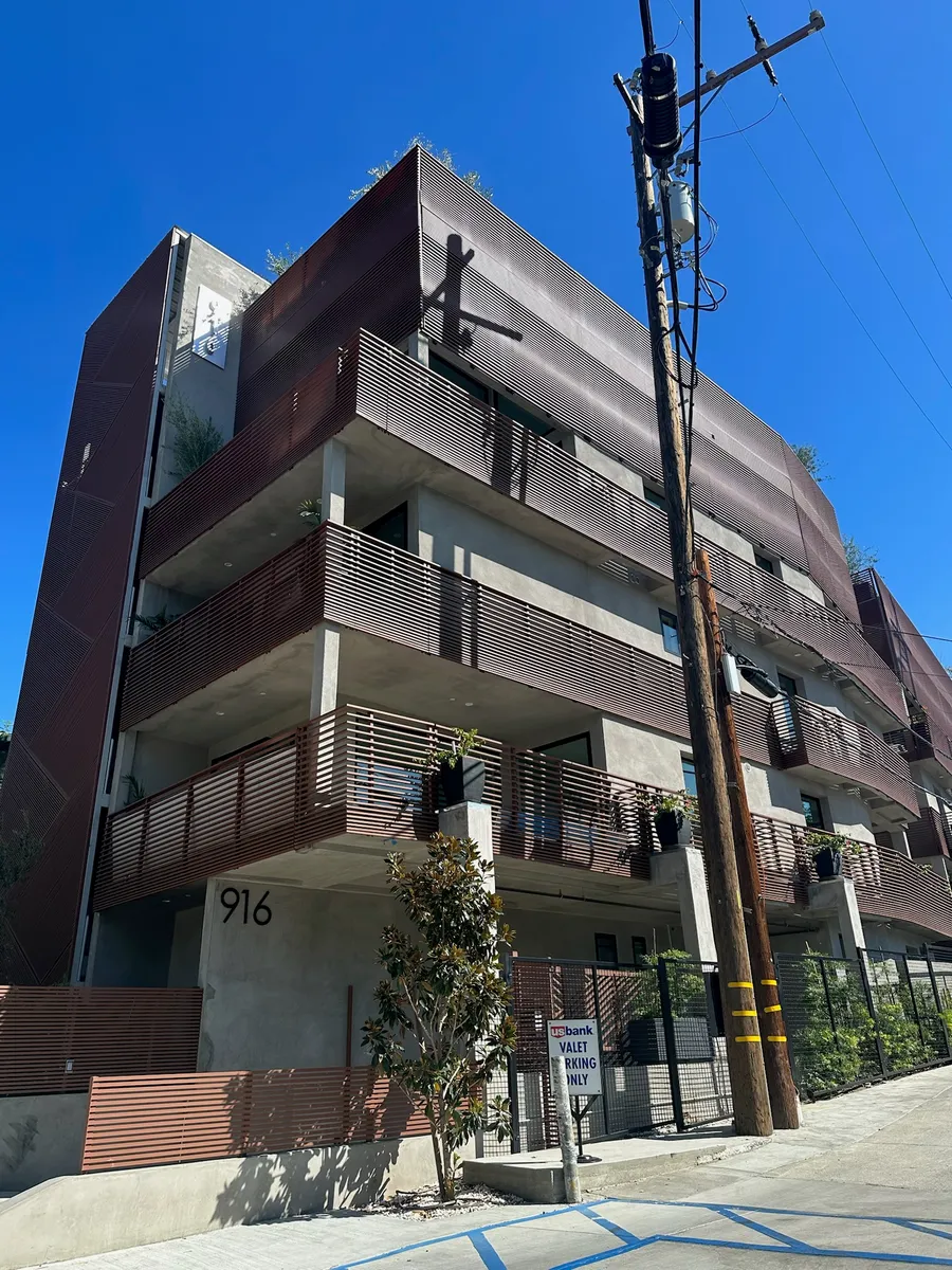 A four-storey apartment building clad in bronze perforated aluminum, with matching horizontal slat screens across every balcony.
