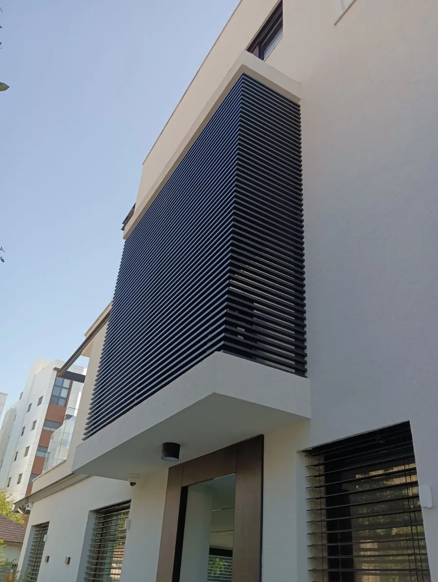 A dark aluminum louvre screen wrapping the corner of an upper floor above a building entrance.