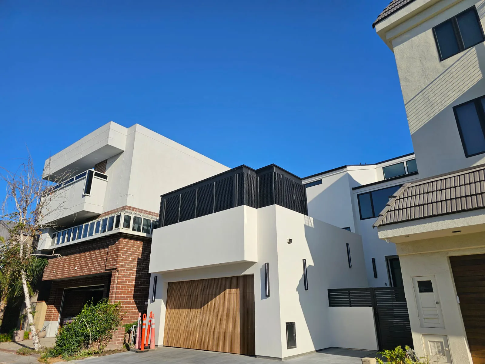 A black aluminum louvre screen enclosing a roof-level volume above a white modern house, next to a wood-look garage door.