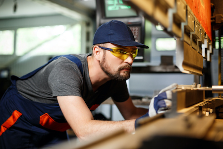 Portrait of worker near metalworking machine, aluminum factory background.